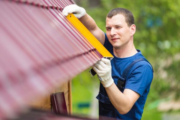 Worker Taking Measurement Of Roof