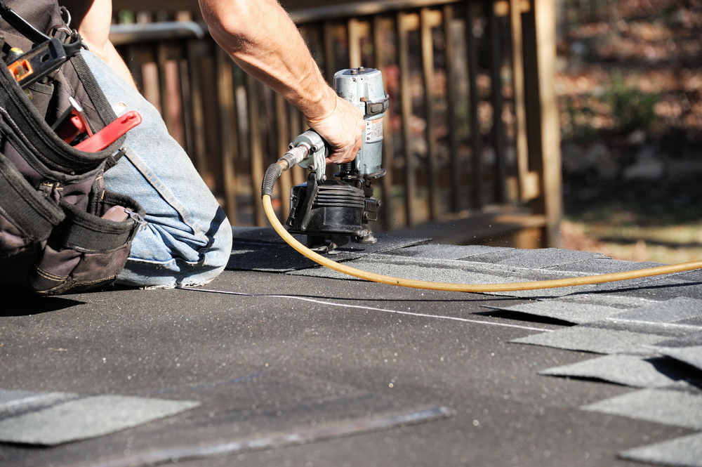 Handyman Using Nail Gun To Install Shingle To Repair Roof